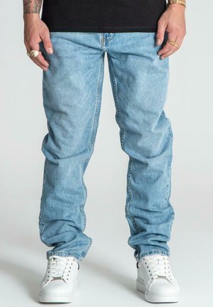 Lichtblauwe denim jeans met een rechte pijpdesign, voorzien van zijzakken en een ritssluiting, gecombineerd met witte sneakers.