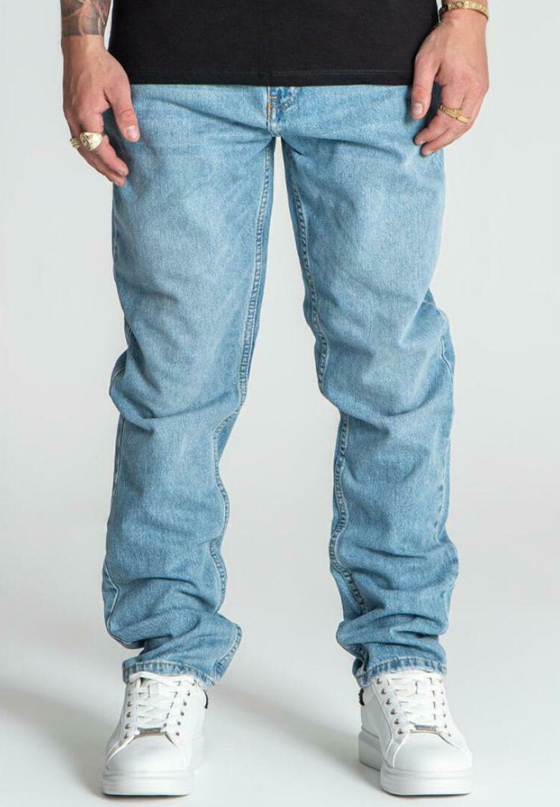 Jeans di denim azzurro chiaro con design a gamba dritta, dotati di tasche laterali e zip, abbinati a sneakers bianche.