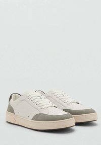 Adidași albi cu accente de suede gri deschis, vârf rotund, cutie perforată pentru degete și talpă de cauciuc bej. Șireturi albe și detaliu subtil de călcâi maro.
