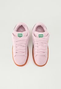 Baskets Puma avec une tige en daim rose doux, bout rond, lacets épais et semelle en caoutchouc marron. Présente une étiquette logo verte sur la languette.