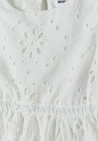 Vestido de algodón blanco con intrincados patrones bordados y detalles recortados. Tiene un escote redondeado y una cintura fruncida. Textura suave.