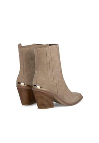 Botas de tobillo de ante beige con punta afilada, costuras verticales y un acento metálico en el tacón. Tacón cuadrado de madera texturizada.