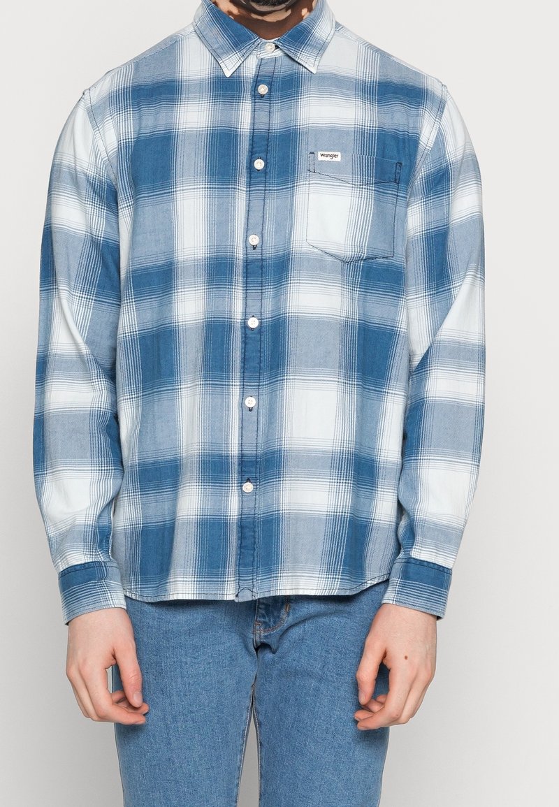 Chemise à carreaux bleue et blanche en tissu léger, avec une poche poitrine et un col classique.