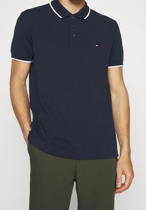 Granatowa koszulka polo wykonana z bawełny, z klasycznym kołnierzykiem, zapięciem na dwa guziki, białymi akcentami na rękawach oraz małym logo na piersi.