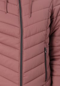Padded jacket w stonowanym różowym kolorze, z pikowaniem w zygzak, zamkiem błyskawicznym z przodu i boczną kieszenią z czarnymi akcentami metalowymi.