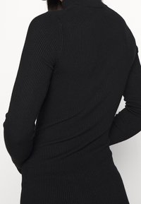 Maglione nero a costine con collo alto e maniche lunghe, che presenta una silhouette aderente con una finitura testurizzata.