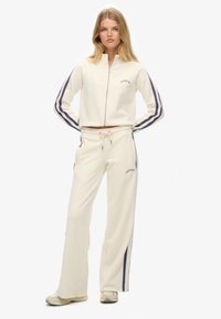 Crème trainingspak met een zip-up cropped jack met paarse strepen en bijpassende sweatpants met een tailleband met trekkoord en zijzakken.