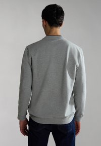Sudadera gris con cuello redondo, mangas largas y puños acanalados. Textura suave, corte casual y una pequeña etiqueta de marca en el dobladillo.