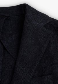 Blazer de lana en espiga de color azul marino oscuro, con cuello y solapas, tejido visible y detalles de costura definidos.