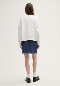 Hvit oversized sweatshirt medDropped Shoulders, paret med et blått denimskjørt. Svarte platåsko og hvite ankelstrømper fullfører antrekket.