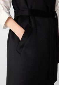 Schwarz-grauer Wollmischung-Artikel mit Taillengürtel, Seitentasche und einer glatten Textur. Verfügt über ein geschichtetes Design mit sichtbarem weißem Ärmel.