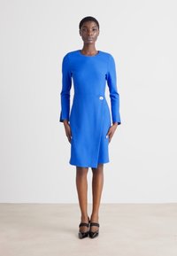 Μπλε, μακρυμάνικο φόρεμα με στρογγυλή λαιμόκοψη, εφαρμοστή σιλουέτα και πλαινό σκίσιμο, με διακοσμητική λεπτομέρεια από κουμπί στη μέση.