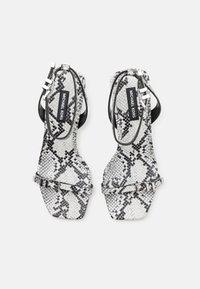 Sandales à talons ouverts à lanières en python noir et blanc avec des boucles en argent et un talon plat. Marque sur la semelle intérieure.