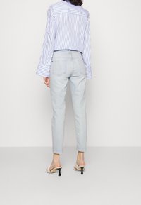 Jeans de corte slim en azul claro, con bolsillos traseros, combinados con una camisa de manga larga a rayas azul y blanca y sandalias de tacón de color claro.