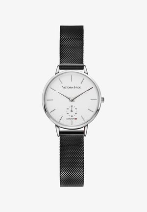 Montre ronde en argent avec un cadran blanc, bracelet en maille noire, indices minimalistes et sous-cadran pour les secondes. Nom de la marque affiché en haut.