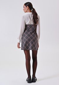Schwarz-beige karierte Kleid mit puffärmel, das einen hohen Kragen hat. Durchsichtige schwarze Strumpfhosen und klobige schwarze Schuhe runden das Outfit ab.
