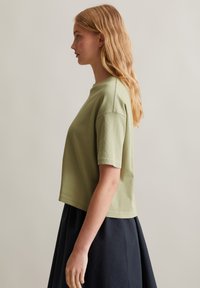 Olijfgroene ribbed t-shirt met korte mouwen, ronde halslijn en een cropped fit, gecombineerd met een donkere uitlopende rok. Soepele textuur.