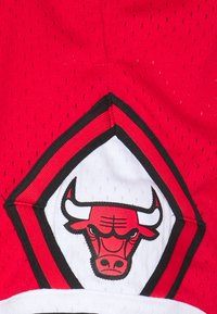 Tejido de malla rojo con un logo en forma de diamante. El logo presenta una cabeza de toro estilizada en rojo y negro, contorneada en blanco.