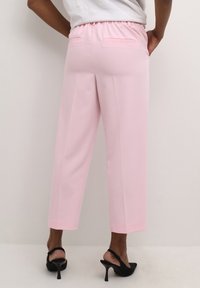 Roze op maat gemaakte broeken met een ontspannen pasvorm, elastische tailleband, cropped lengte en twee achterzakken. Gecombineerd met zwarte strappy hakken.