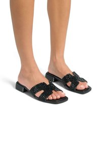 Chanclas negras con un empeine texturizado de cuentas y diseño entrecruzado, base cuadrada brillante y tacón bajo.