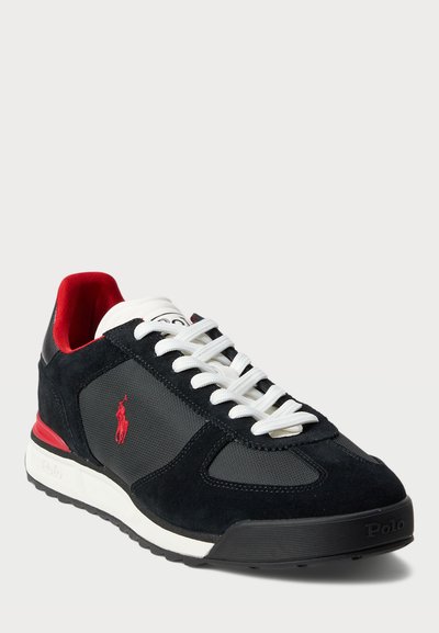 Juodos suedingos ir tinklelio sportinės bateliai su raudonais akcentais, baltais raišteliais ir guminėmis padangomis. Šone yra logotipas ir paminkštinta apykaklė.