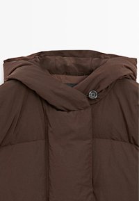 Bruine pufferjas met een capuchon, voorzien van een knoopsluiting en een gladde, zachte textuur. Het ontwerp bevat doorgestikte secties voor isolatie.