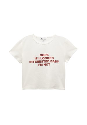 Camiseta corta blanca de algodón. Presenta un texto rojo: "OOPS SI PARECÍA INTERESADA, NENÉ, NO LO ESTOY." Mangas cortas y escote redondo.