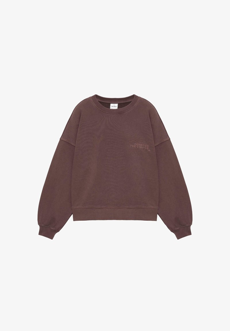 Sweat-shirt marron col rond à manches longues avec poignets côtelés, comportant un petit texte « DESIGNED FOR CHANGE » sur la poitrine gauche.