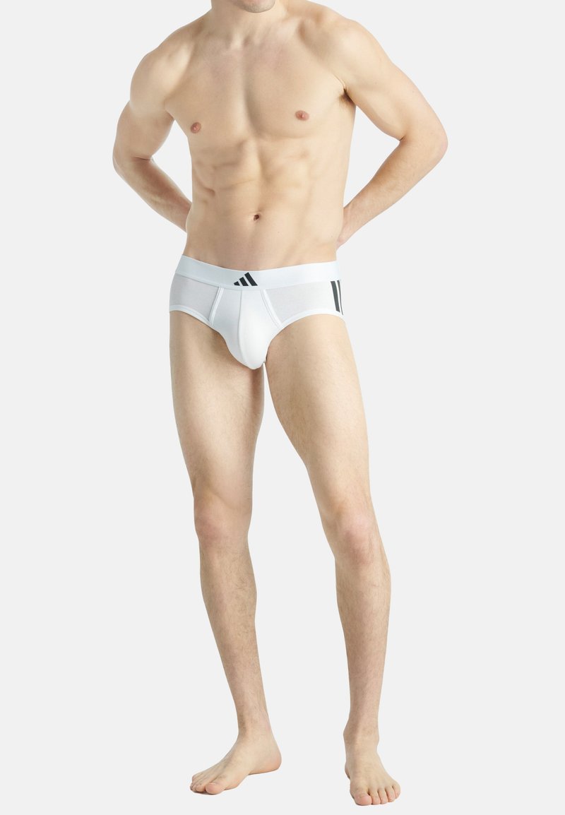 Vita bomullstrosor med en tight passform, kontrasterande svarta sidostråk och elastiskt midjeband med logodetaljer. Slät textur, minimal design.