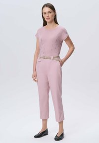 Jasnoróżowa bluzka z krótkim rękawem w kwiatowy wzór, zestawiona z jasnoróżowymi spodniami 3/4 i plecionym beżowym paskiem; czarne mokasyny.