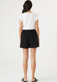 Top blanco de manga corta con mangas de volantes y textura de ojales, combinado con pantalones cortos negros con cinturilla elástica y un diseño texturizado.