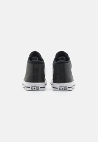 Sneakers înalte din piele neagră cu talpă din cauciuc alb, având un patch cu logo și cusături contrastante pe spate. Design clasic.