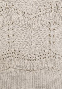 Pull en tricot de couleur beige clair avec des motifs ajourés complexes et des bords côtelés. Présentant des sections de textures variées et une finition douce.