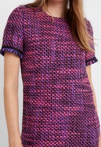 Kraťasový top v tkaném vzoru fialové, růžové a černé barvy. Má třásňové manžety a kulatý výstřih, s texturovaným povrchem.