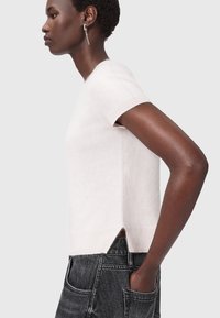 Maglione corto rosa chiaro a maniche corte in morbido materiale, caratterizzato da un taglio dritto con spacchi laterali, abbinato a jeans blu scuro.