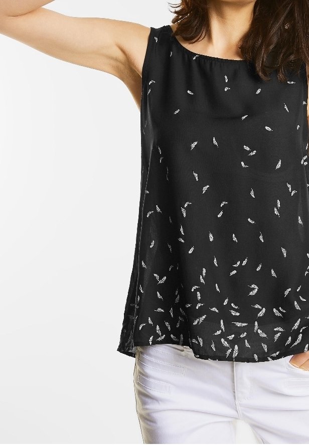 Femme portant un haut noir sans manches avec de petits motifs de plumes blanches et un pantalon blanc, bras levé.