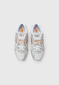 Baskets de course en mesh blanches avec des accents argentés, des détails orange et des lacets blancs. Elles présentent une semelle rembourrée et un design respirant.