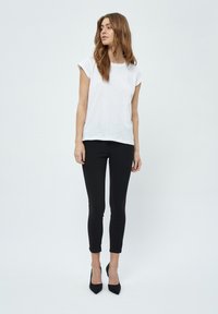 T-shirt bianco a maniche corte abbinato a leggings neri aderenti e décolleté neri a punta, caratterizzato da un design semplice e pulito e una morbida texture.