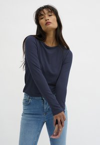Navy long-sleeve shirt with a round neckline, paired with light blue skinny jeans. Smooth texture, fitted design, minimalistic style.