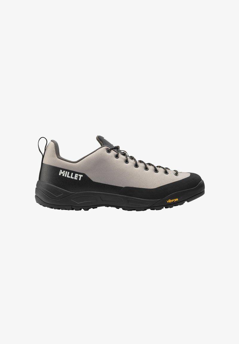 Chaussure de randonnée Millet beige clair et noire avec des lacets noirs, semelle Vibram et languette au talon, vue de côté.