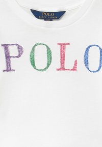 Bílá bavlněná tričko s nápisem "POLO" v několika barevných, křídovém stylu: fialové, zelené, červené a modré. Hladká textura, kulatý výstřih.