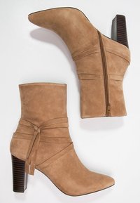 Botas de tobillo de ante color beige con punta afilada, correas envolventes y cremallera lateral; cuenta con un tacón de bloque de madera texturizada.