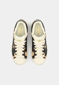 Baskets Adidas avec un dessus en imprimé léopard noir et beige, des lacets crème et un embout texturé. Présente un logo doré sur la languette.