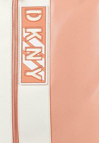 Bolso DKNY que presenta una combinación de cuero melocotón y crema, con un destacado logo de DKNY en naranja sobre un parche blanco y un zipper a juego.