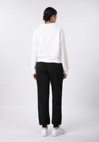 Λευκό φούτερ με γιακά, σε συνδυασμό με μαύρο παντελόνι άνετης γραμμής. Το μοντέλο φοράει λευκά αθλητικά παπούτσια. Ομαλές υφές και καθημερινός σχεδιασμός.