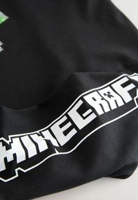 Čierne tričko s krátkym rukávom s bielym logom "Minecraft". Textúra je hladká s jemným povrchom a dizajn je odvážny a grafický.
