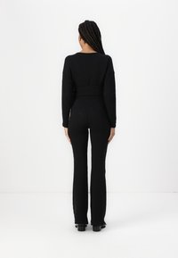 Svart strikket jumpsuit med et teksturert diamantmønster, lange ermer, en tilpasset midje og flagrende bukser. Glatt stoff med ensfarget design.