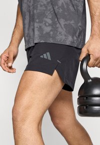 Μαύρο αθλητικό σόρτς με σκίσιμο στο τελείωμα, κατασκευασμένο από ελαφρύ ύφασμα. Διαθέτει γκρι διαγώνιο σχέδιο με ρίγες και λογότυπο στο πλάι.