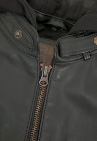 Schwarze Lederjacke mit Reißverschluss und Details aus Messing. Weiche Stoffauskleidung ist am Kragen sichtbar.