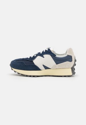 Lavskaftet sneaker med marineblåt ruskind, hvide teksturerede læderpaneler, beige hæl, cremefarvet mellemsål og sort nittet gummisål, sideperspektiv.